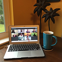 An I T C C video call takes place on a laptop sitting on a tabletop next to a cup of tea. Students communicate with each other on screen.